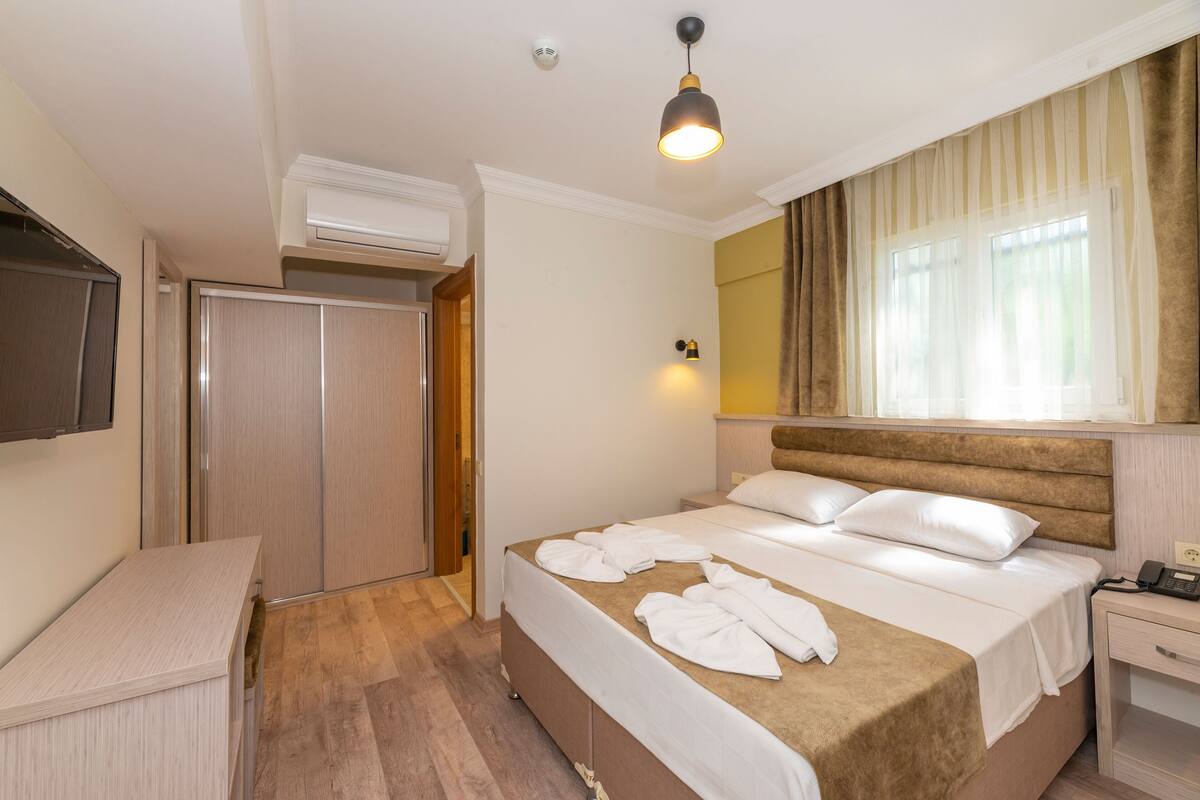 A hotel room with a bed, bedside table, and a TV mounted on the wall.
