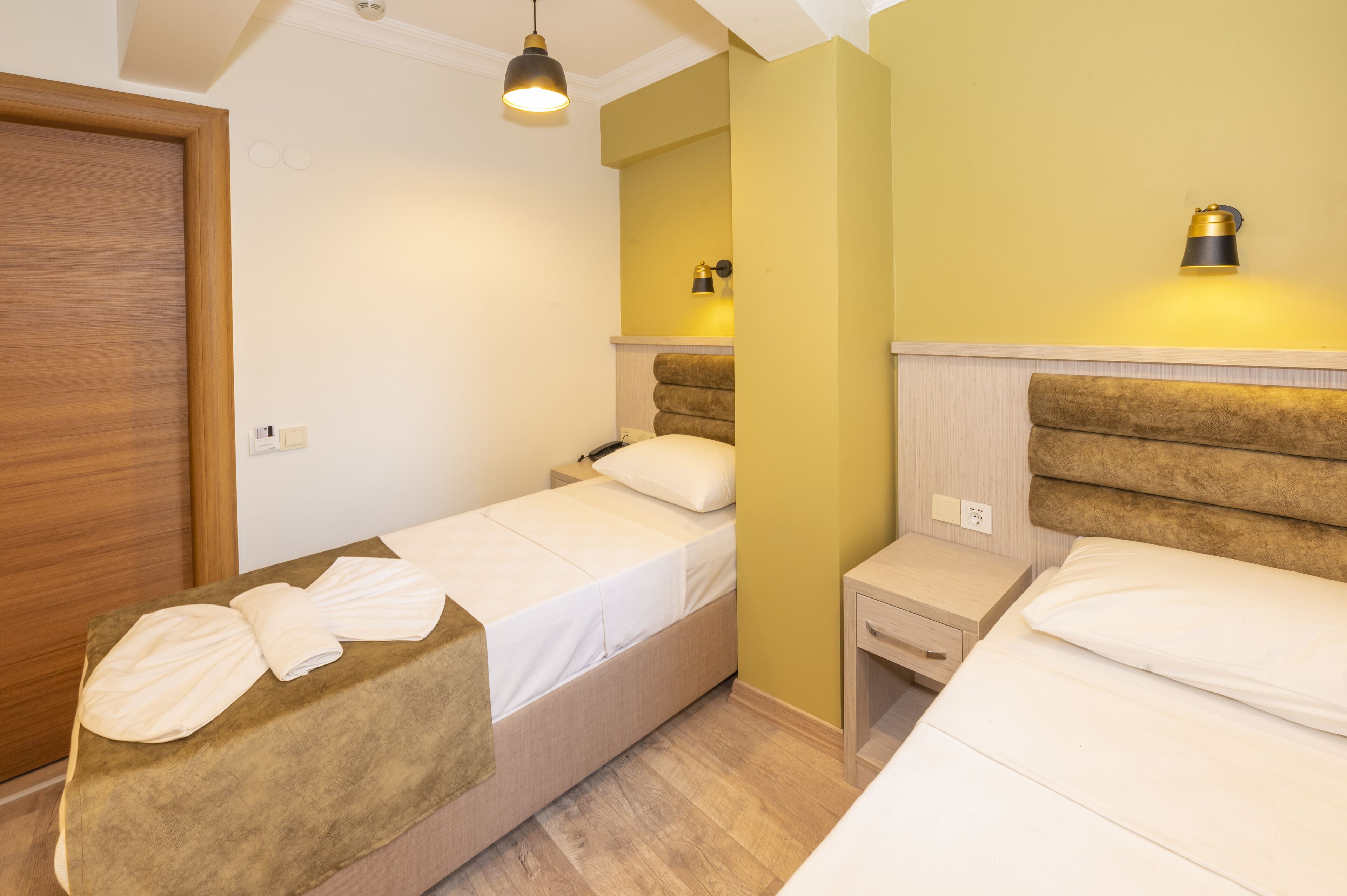 A twin room with two beds, a wooden wardrobe, a bedside table, a nightstand, and a wall-mounted lamp.