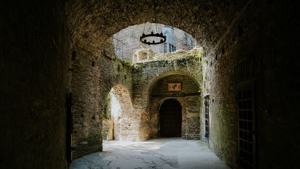 Un corridoio in pietra stretto, con un arco e un lampadario.