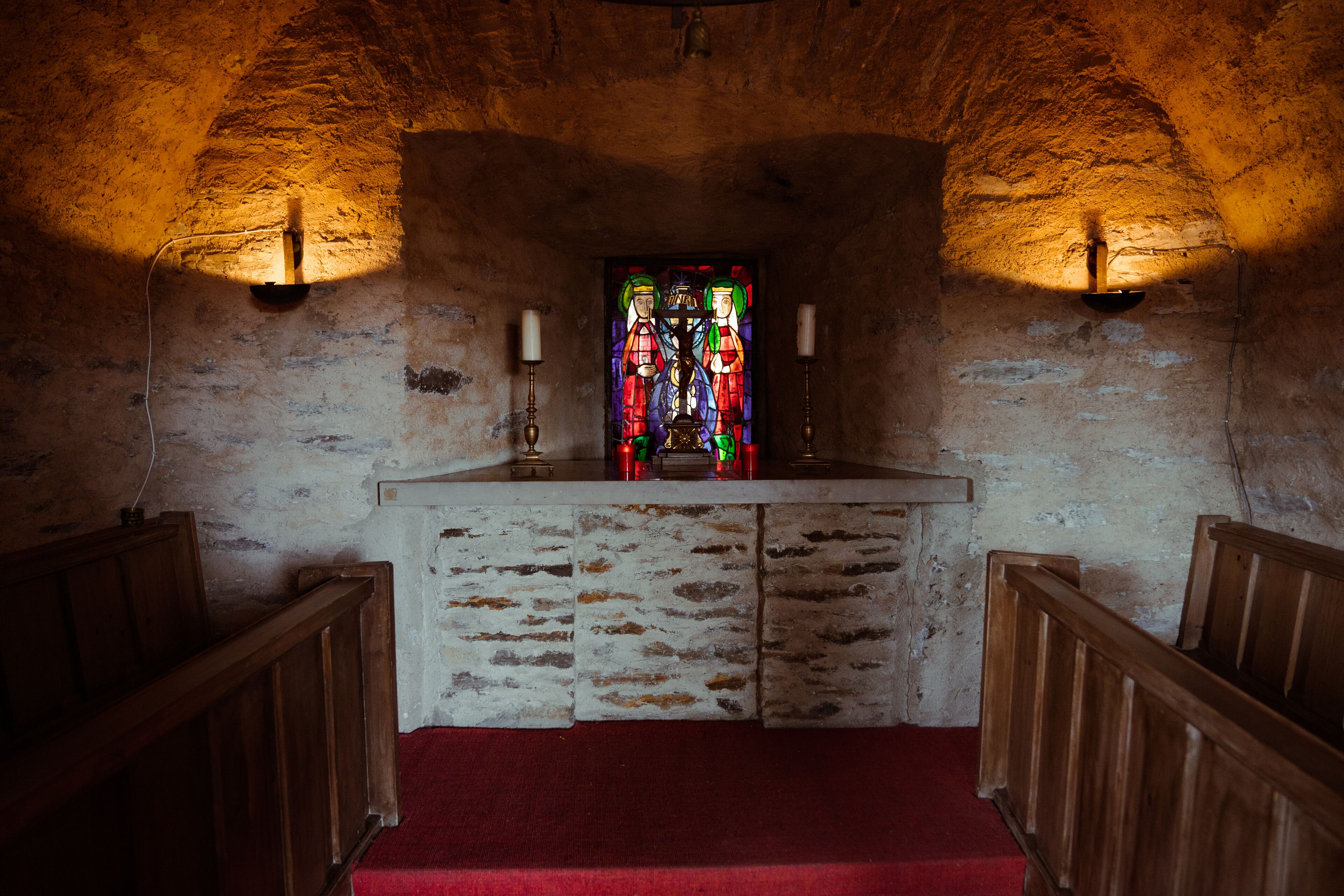 A church interior with a wooden altar, pews, and a stained glass window.