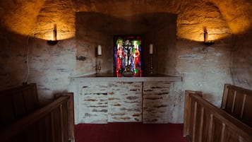 A church interior with a wooden altar, pews, and a stained glass window.