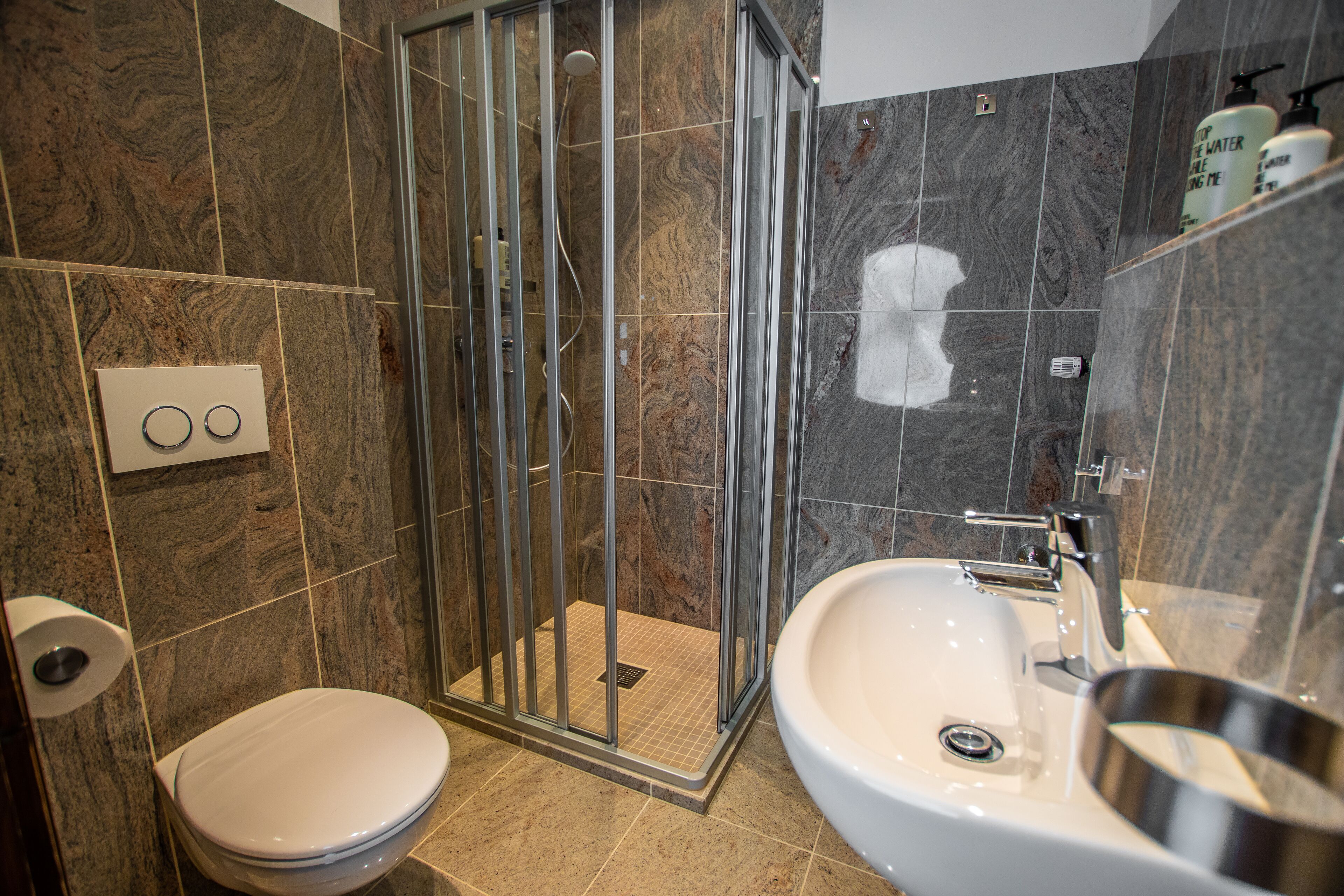 A bathroom with a shower enclosure, toilet, sink, and marble tiles.