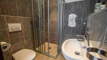 A bathroom with a shower enclosure, toilet, sink, and marble tiles.