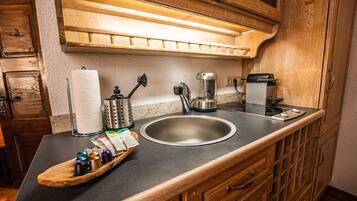 A kitchen with a stainless steel sink, wooden cabinets, a coffee maker, and a tray with coffee pods.