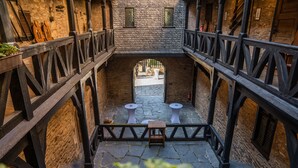 Un cortile con pavimento in pietra, ringhiere in legno e due tavoli bianchi.