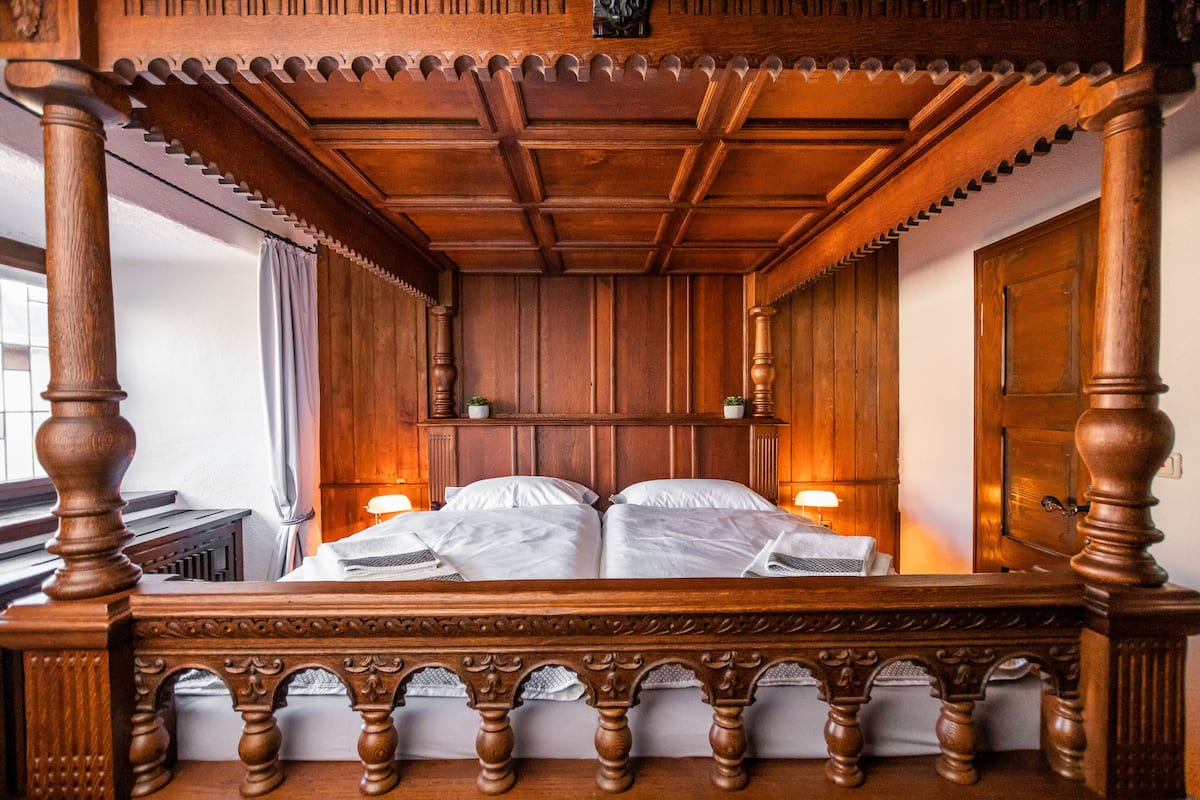 A four-poster bed with a wooden canopy, a nightstand with a lamp, and a wooden door.
