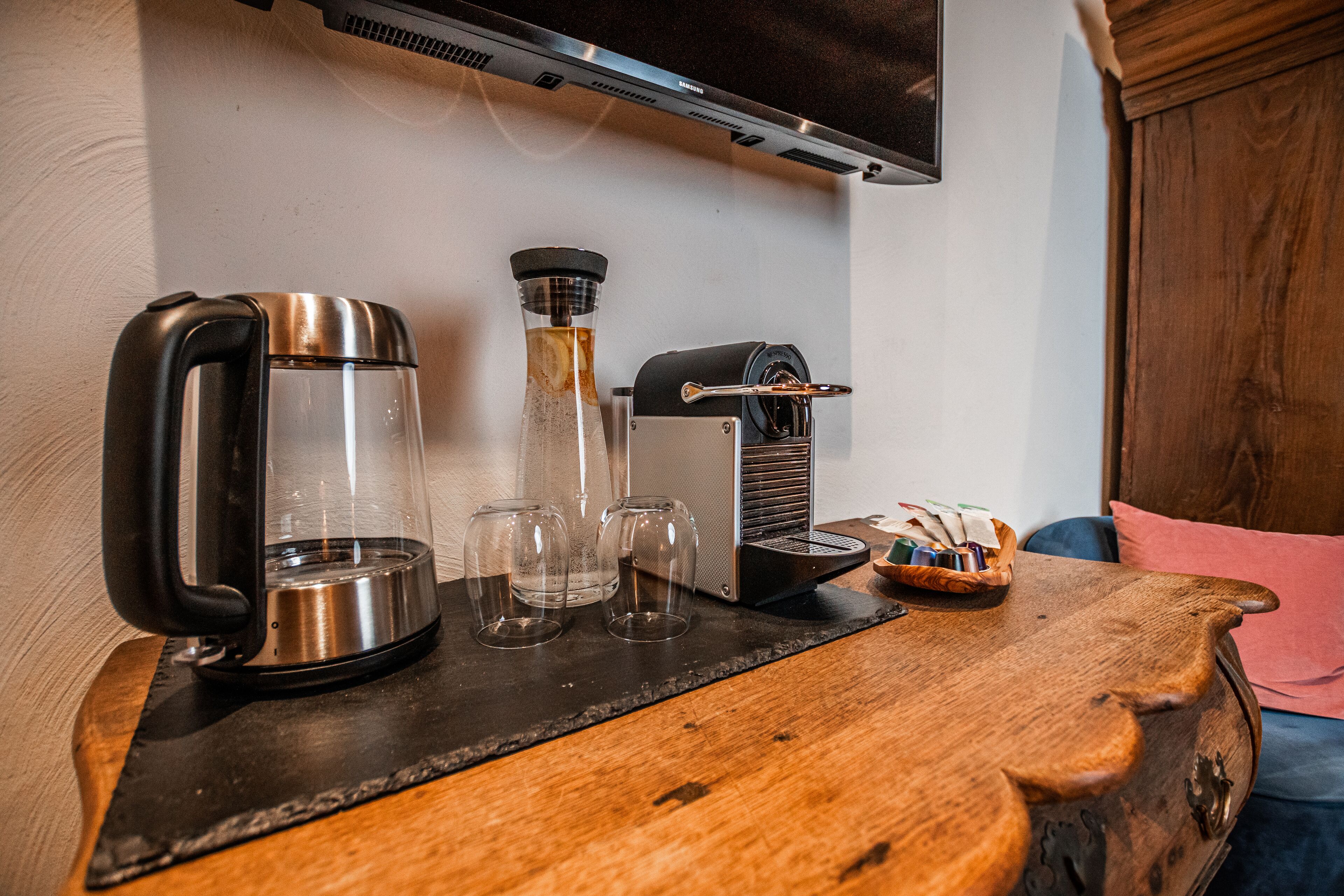 Una cafetera, una jarra de vidrio y tres vasos sobre una mesa de madera.
