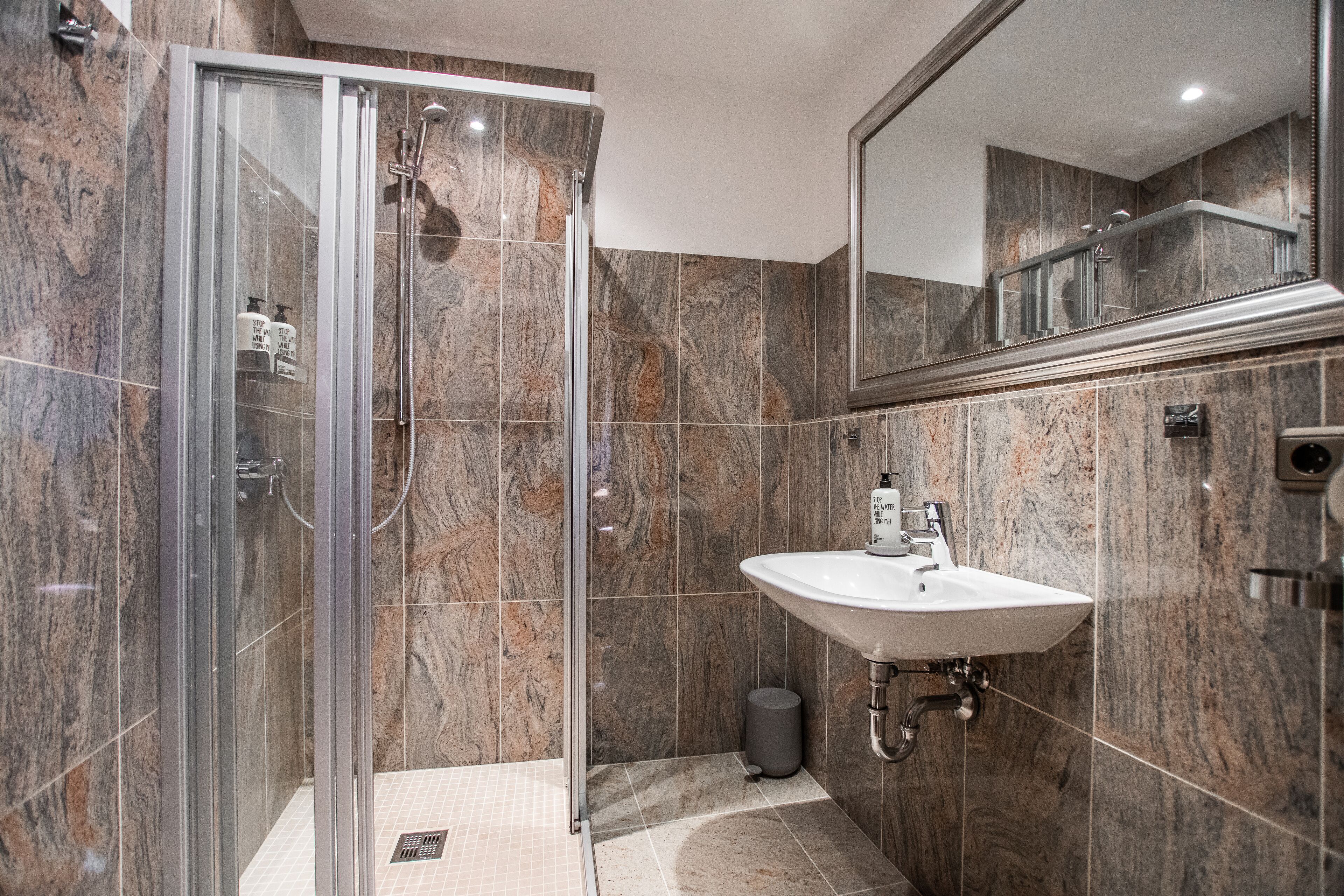 A modern bathroom with a glass-enclosed shower, a white sink, and a marble-tiled wall.