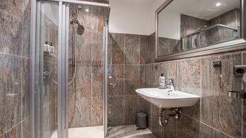 A modern bathroom with a glass-enclosed shower, a white sink, and a marble-tiled wall.