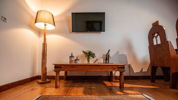 Una mesa de madera con una lámpara, un televisor de pantalla plana y una silla de madera decorativa en una habitación con piso de madera y un tapete estampado.