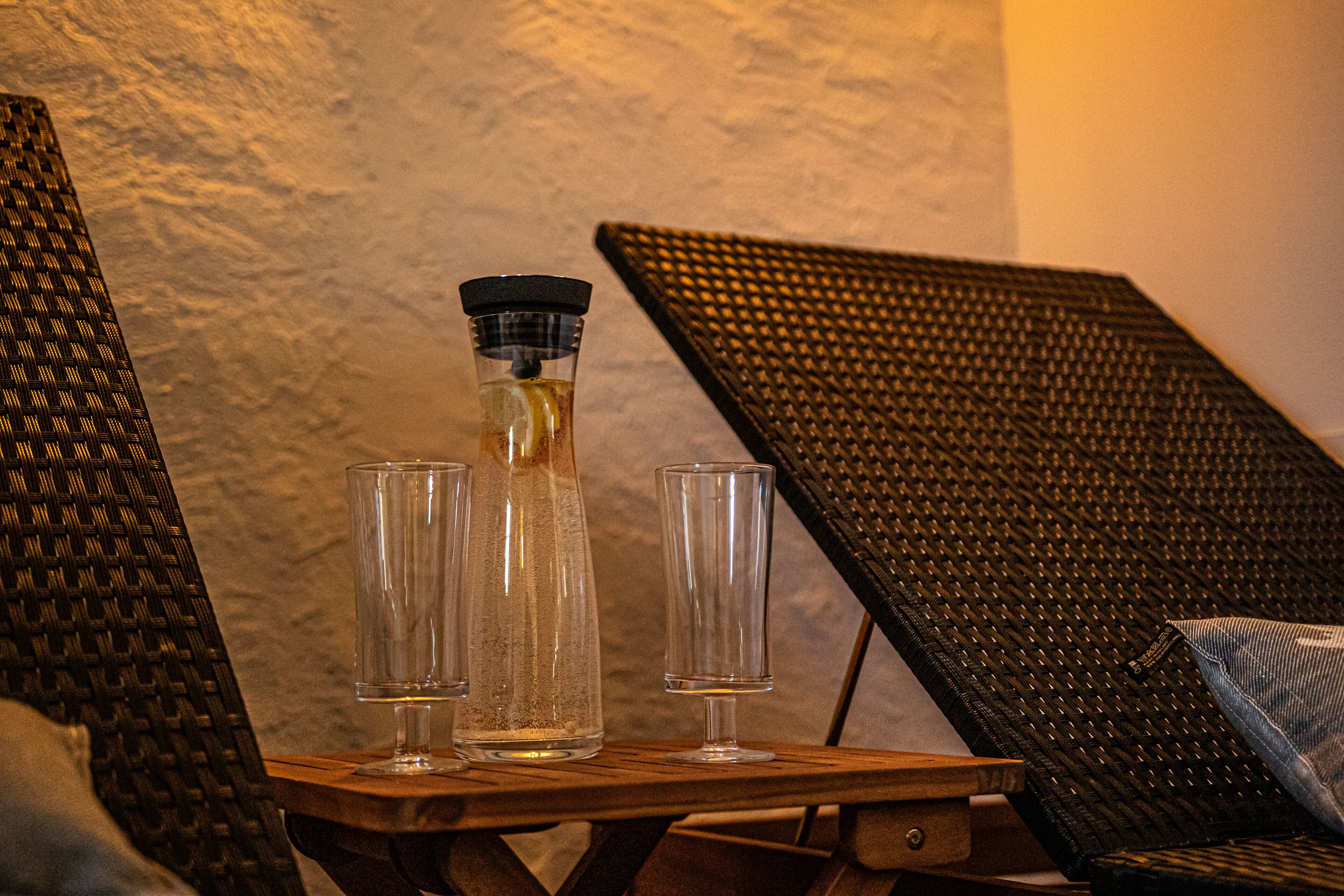 A wooden table with a bottle and two glasses, set against a textured wall.