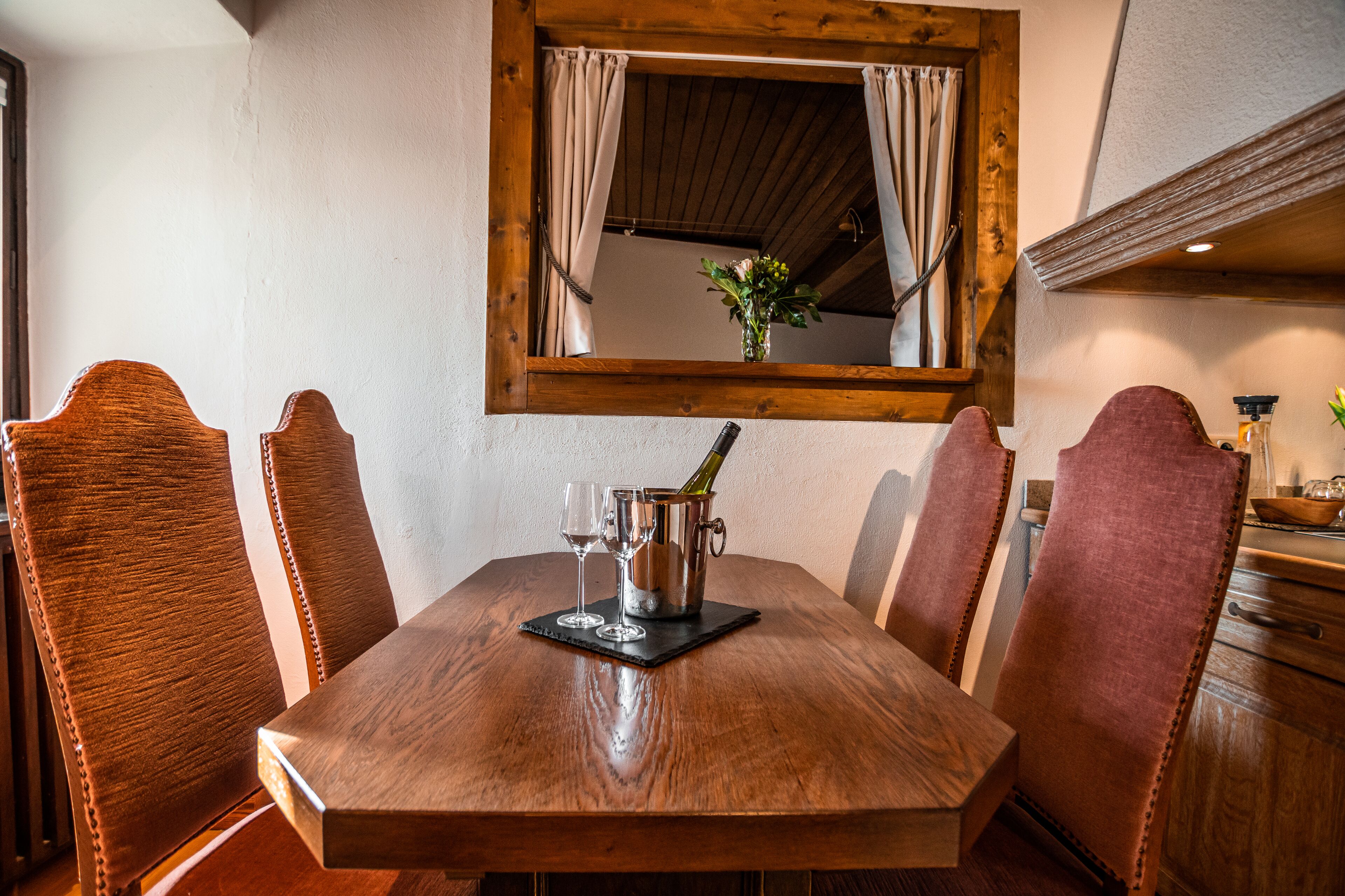 A wooden dining table with a wine bottle, two glasses, and a small vase with flowers.