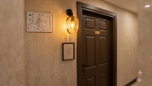 Una porta marrone con una targa, una pianta in vaso e un punto luce fissato al muro.