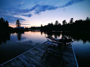 A wooden dock extending into calm water with a chair and a small table, surrounded by trees and a clear sky. - Getaway with Snowmobile, ATV, and boating access!! (Rockwood)
