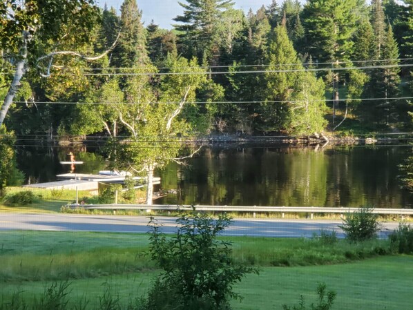 A serene lakeside view with a dock, surrounded by lush greenery and a bridge in the background. - Getaway with Snowmobile, ATV, and boating access!! (Rockwood)
