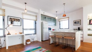 A modern kitchen with a central island, bar stools, pendant lighting, and a colorful rug. - MIKLAT Luxury Condo & Spectacular View by FeelHome (Tel Aviv - Jaffa)