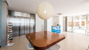 Un hall d’hôtel moderne avec une table en bois, un comptoir d’accueil et un grand luminaire suspendu.