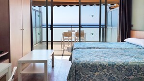 Une chambre d’hôtel avec un lit, une petite table, une chaise et un balcon donnant sur la mer.