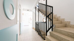 Un couloir avec un mur bleu clair, un élément décoratif circulaire au mur et un escalier avec des marches de couleur beige et des rampes noires.