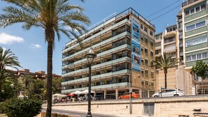 Ein mehrstöckiges Gebäude mit Balkonen, einer Palme und einer Straße mit parkenden Autos.