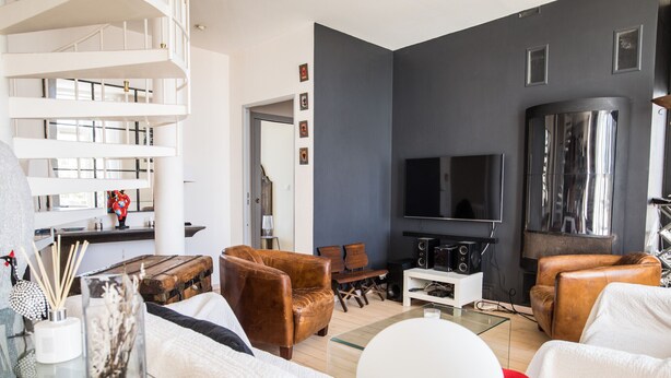 Una sala de estar moderna con escaleras, sofás de cuero, un televisor de pantalla plana y una mesa de centro de vidrio.