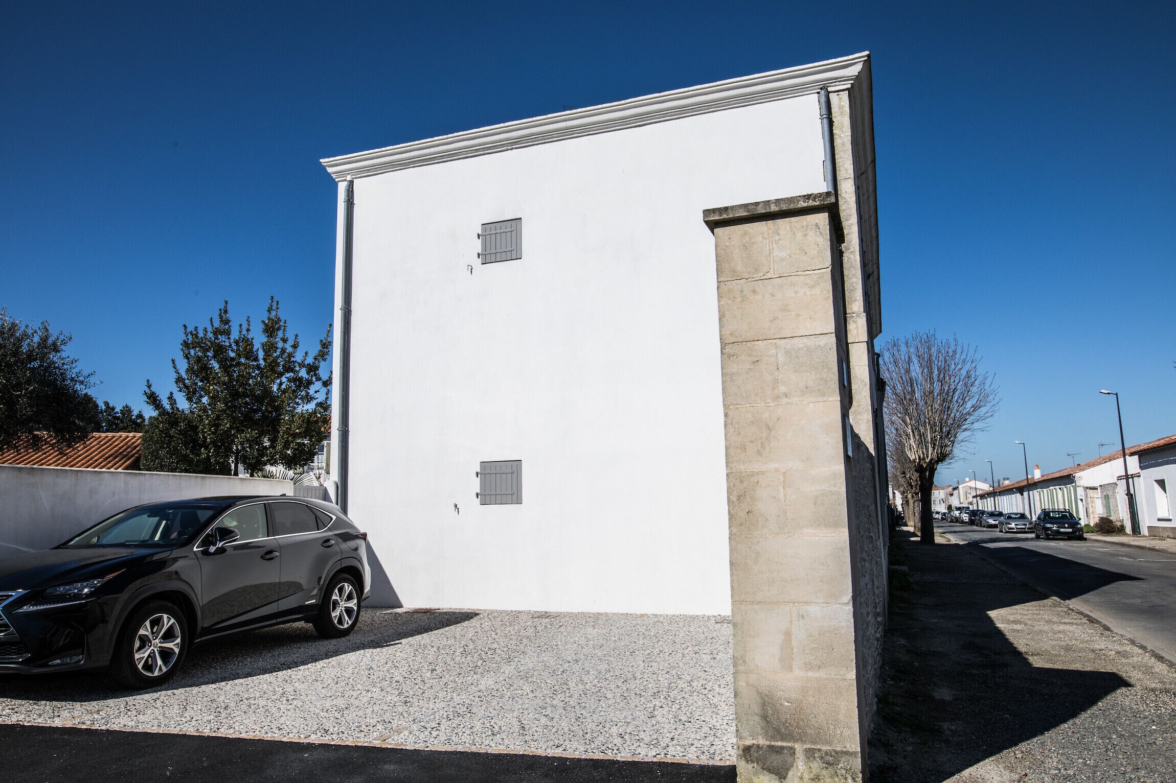 A modern building with a white facade, a parked SUV, and a clear blue sky.