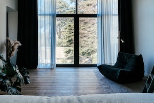 A room with a large window, a dark green bean bag chair, and a potted plant.