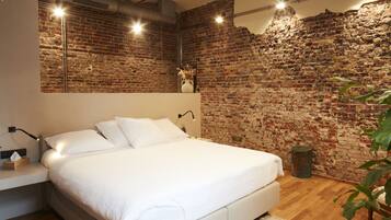 A modern bedroom with a brick wall, a large bed, bedside lamps, and a wooden floor.