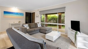 A modern living room with a sectional sofa, a flat-screen TV, and a large window offering a view of greenery. - This revamped quintessential holiday home, prime location (sleeps 8) (Sorrento)