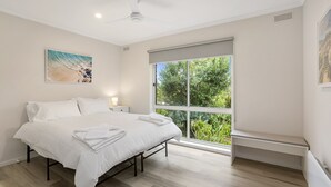A bedroom with a bed, a nightstand, a ceiling fan, a window with a view of greenery, and a painting on the wall. - This revamped quintessential holiday home, prime location (sleeps 8) (Sorrento)
