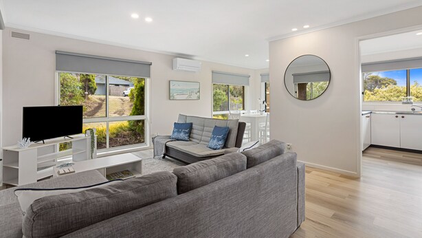 A modern living room with a grey sofa, a flat-screen TV, and a dining area with a kitchen in the background. - This revamped quintessential holiday home, prime location (sleeps 8) (Sorrento)