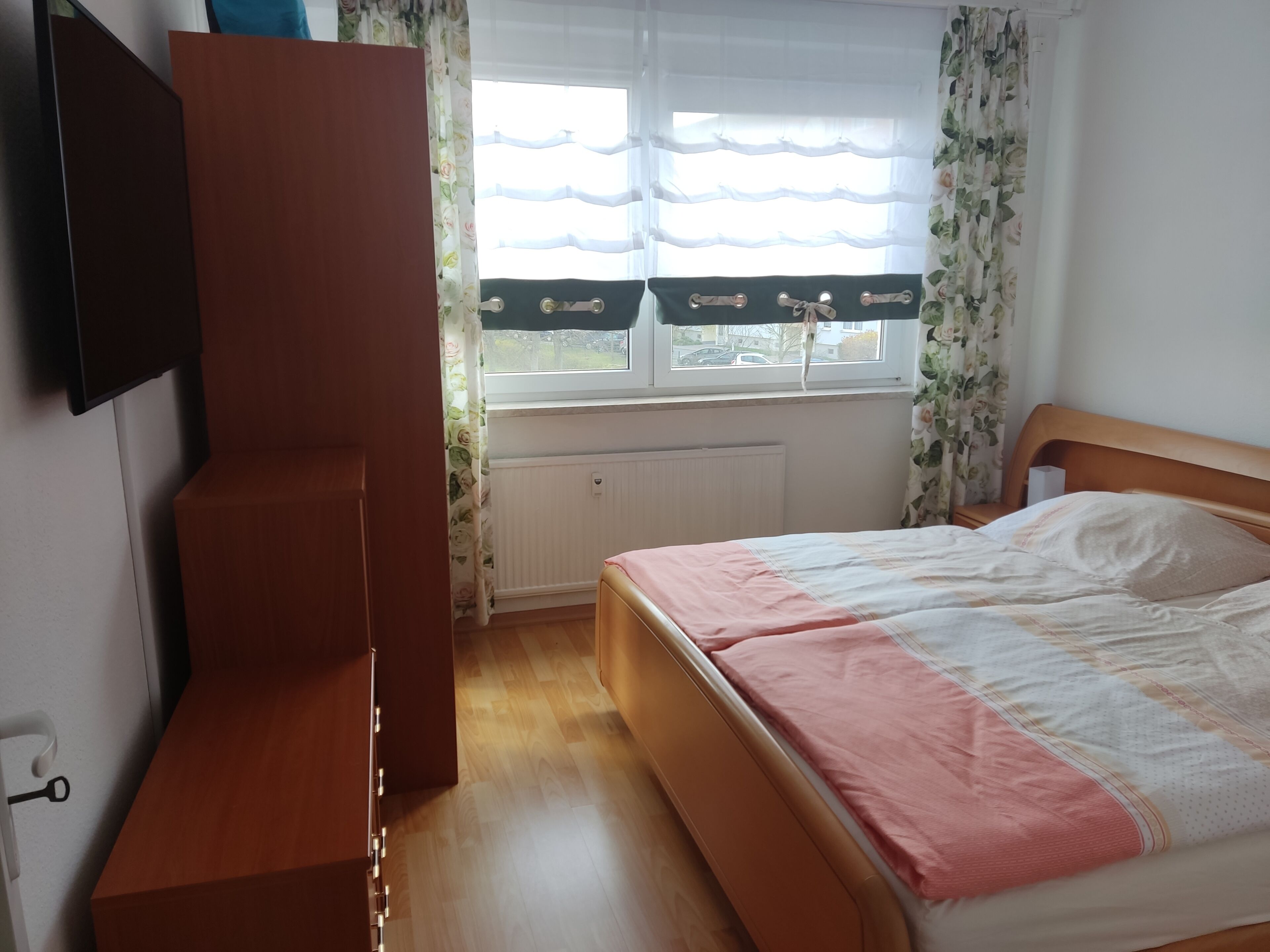 A bedroom with a bed, wooden wardrobe, and a window with curtains.