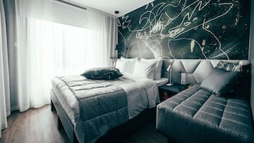 A modern hotel room with a bed, a sofa, a large wall mural, and a window with sheer curtains.