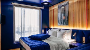 A modern bedroom with a large bed, a bedside table, and a view of the city through a window. - Hotel AX (Helsinki)