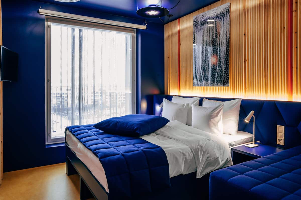 A modern bedroom with a large bed, a bedside table, and a view of the city through a window.
