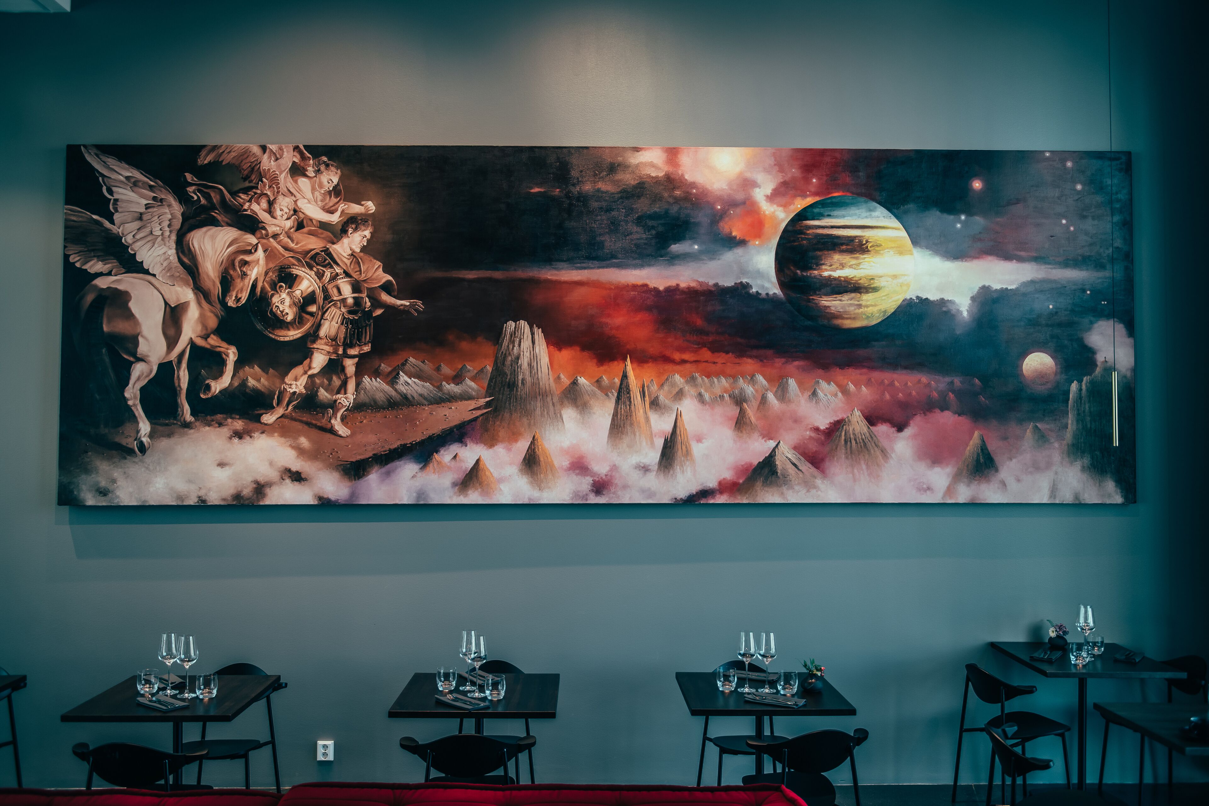 A dining area with tables and chairs, a large painting on the wall depicting a celestial scene, and a red cushioned seating area.