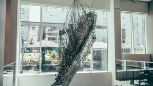 Ein modernes Interieur mit großen Fenstern, einer hängenden Metallskulptur und Blick auf Sitzmöglichkeiten im Freien.