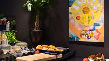 Montaje de bufé con diferentes alimentos, una planta y un cuadro de pared colorido.