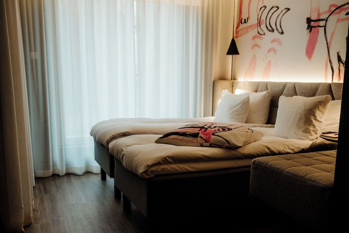 A hotel room with a bed, a sofa, a wooden floor, and a wall with a mural.