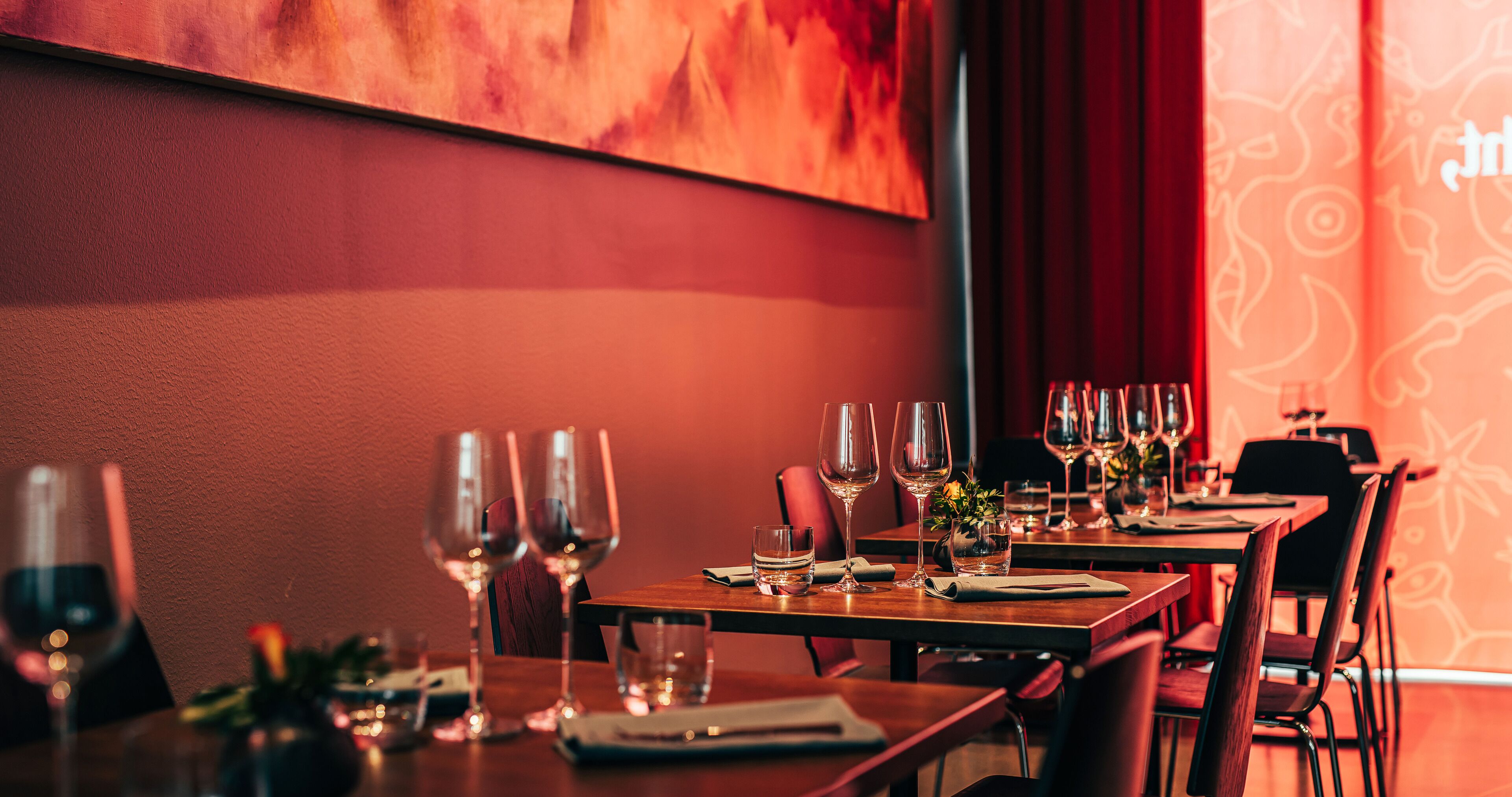 A restaurant interior with tables set for dining, featuring wine glasses and cutlery.