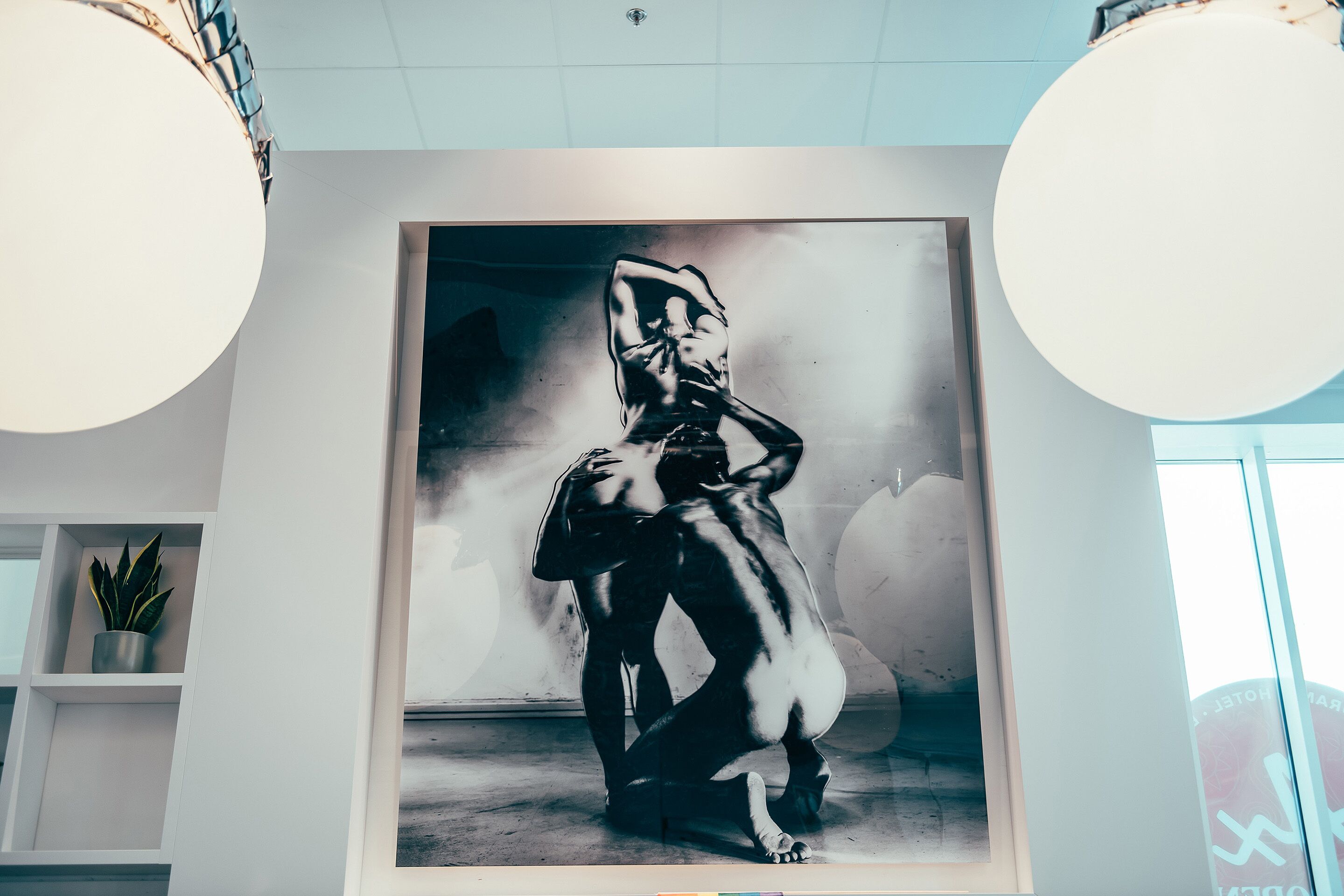 Ein großformatiges Schwarz-Weiß-Kunstwerk zeigt eine Figur in einer dynamischen Pose, präsentiert in einem modernen Raum mit weißen Wänden und schlichter Einrichtung.