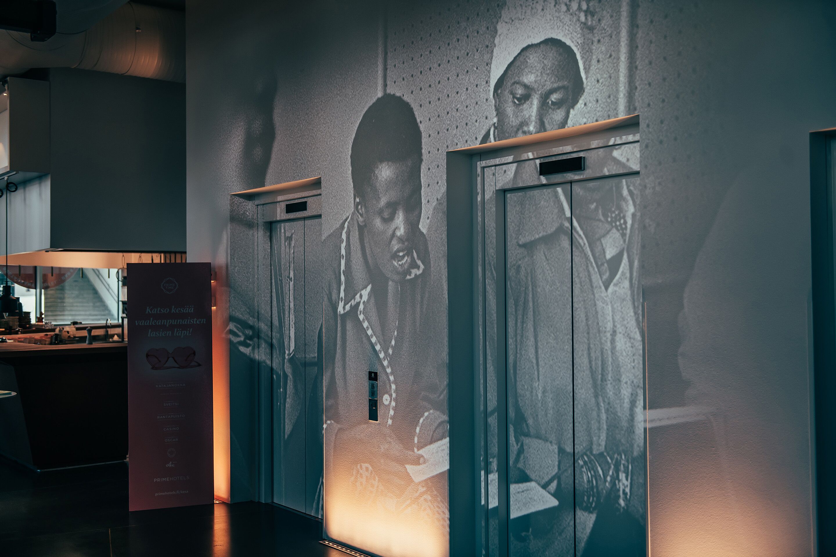 A hallway with a projection of two individuals on the wall, a reception desk, and a sign with text.