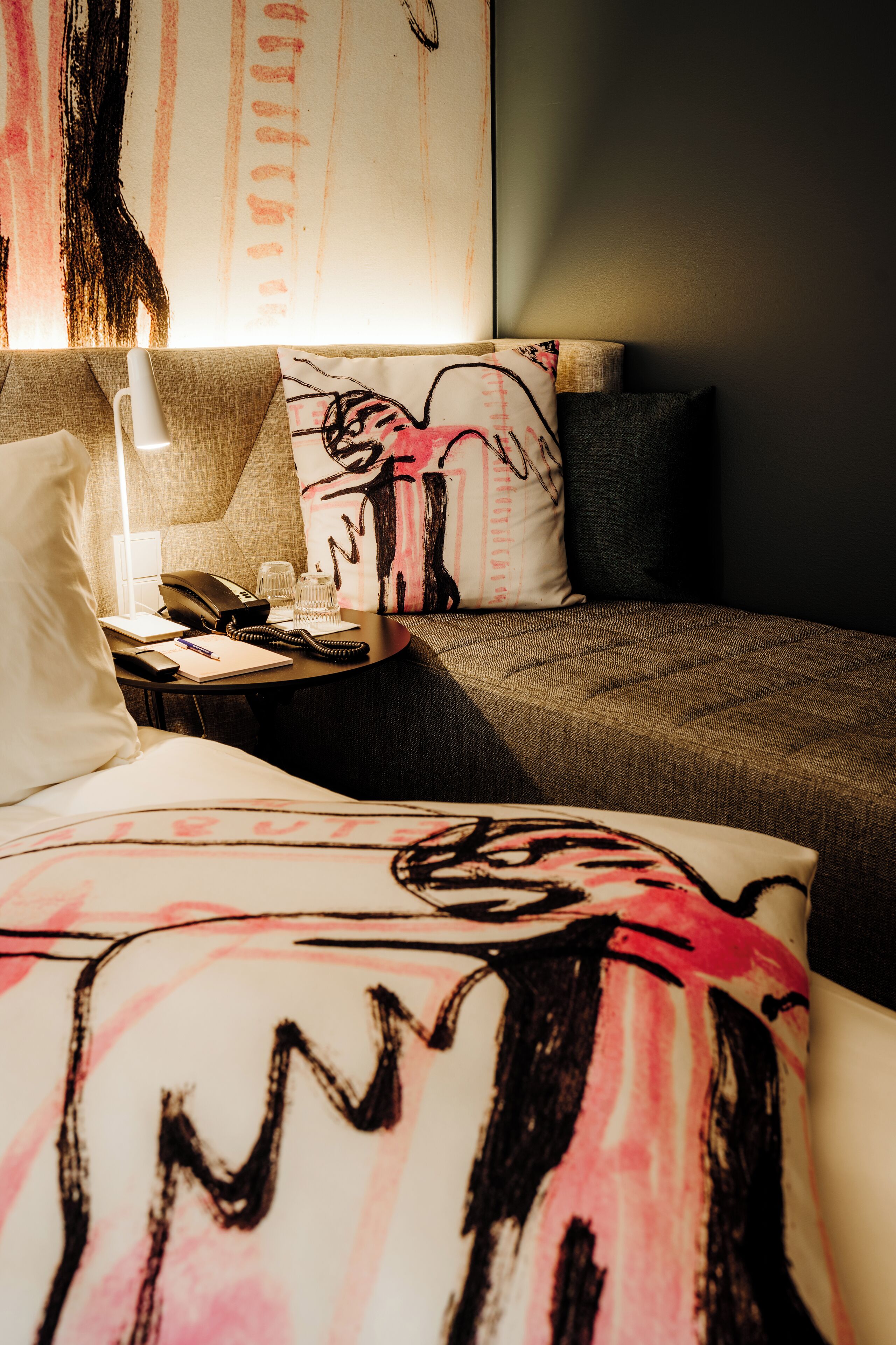 Una habitación de hotel con una cama, una mesita de noche con lámpara, un teléfono y un cuaderno.