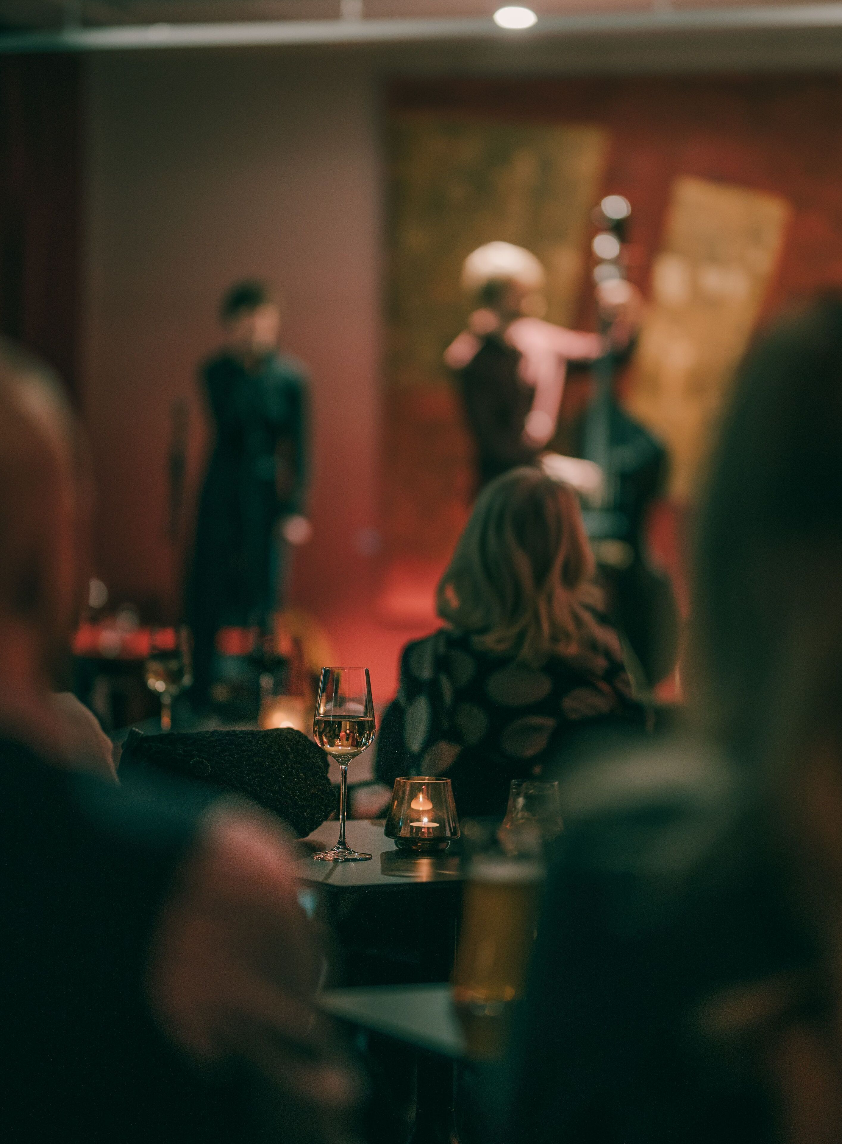 Ein Restaurantinnenraum im schummrigen Licht, mit gedeckten Tischen und Kerzen auf jedem Tisch, im Hintergrund steht eine Person.