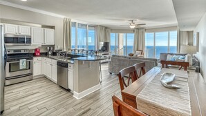 A modern kitchen with a central island, a dining area with a view, and a living room with a sofa and TV.