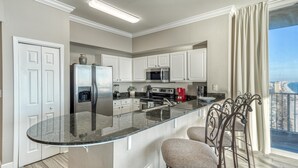A modern kitchen with a central island, white cabinetry, stainless steel appliances, and a view of the city through large windows.