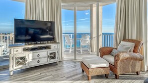 A balcony with a TV, wicker furniture, and a view of the ocean.