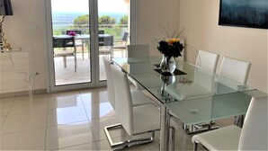 A modern dining area with a glass table and chairs, a vase of flowers, and a view through glass doors to an outdoor patio. - Luxury villa in a privileged location - sea view -private pool - fibre internet. (Palau-Saverdera)
