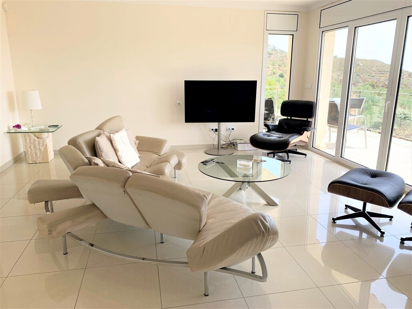 Een moderne woonkamer met een bank, een glazen salontafel, een televisie en een fauteuil.