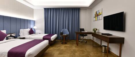 Habitación de hotel con dos camas, un escritorio, una silla, un televisor y un ventanal con cortinas.